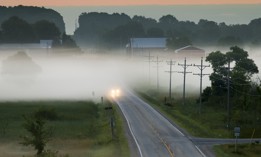A car drives along a road, in morning fog, in Wisconsin.