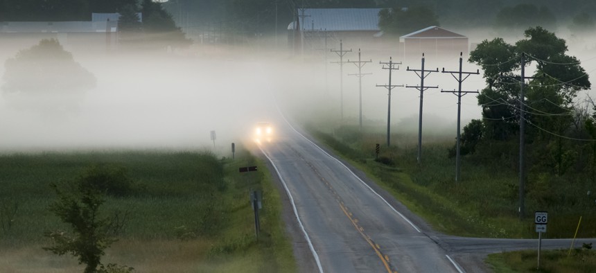 A car drives along a road, in morning fog, in Wisconsin.