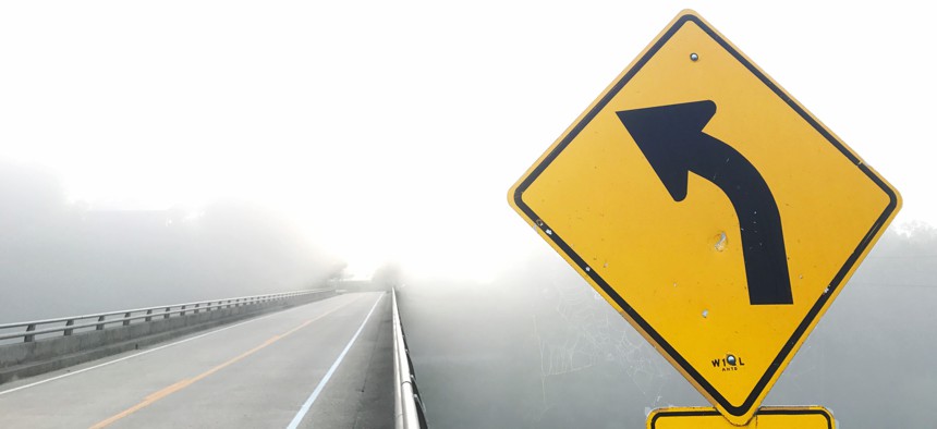 A road sign warning of an upcoming curve on a foggy day.