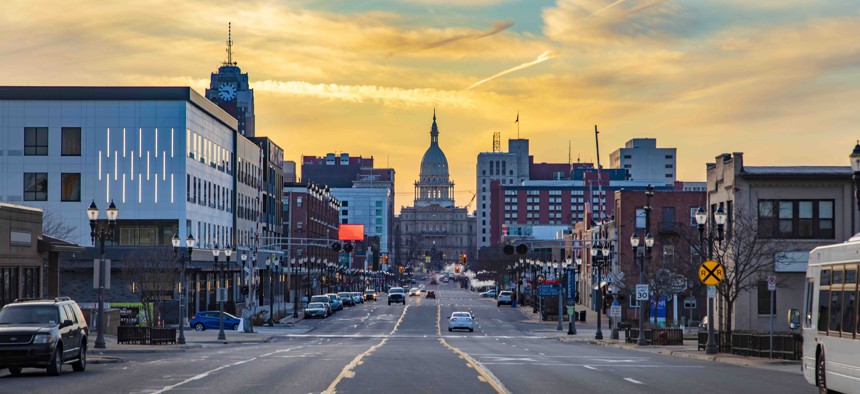 The sun sets over the Michigan state capitol and a wide road leading to it in Lansing.