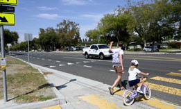 A parent raises an arm as he and his child cross the street at Studebaker Road, leaving an elementary school, where there is no crossing guard posted in Long Beach, California.