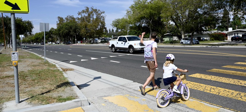 A parent raises an arm as he and his child cross the street at Studebaker Road, leaving an elementary school, where there is no crossing guard posted in Long Beach, California.