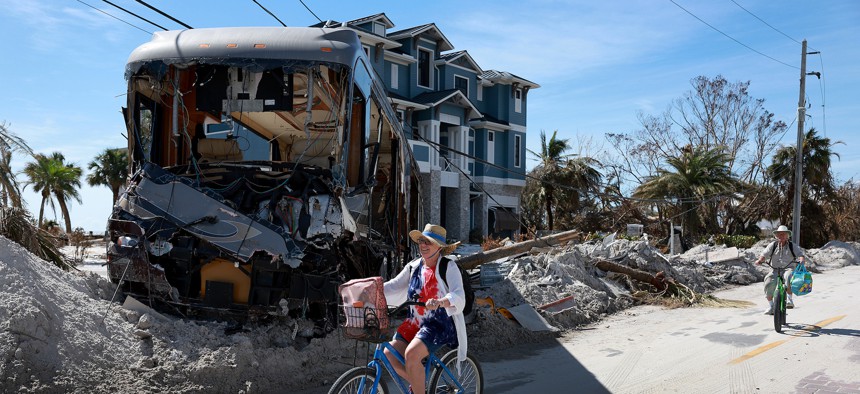 Elizabeth D'Onofrio and Sean Halliday ride their bikes past a destroyed RV in the wake of Hurricane Ian on October 3, 2022 in Fort Myers Beach, Florida. 