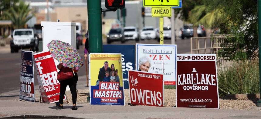 Pedestrians walk by political campaign signs that are posted on a street corner on July 29, 2022 in Phoenix, Arizona. 
