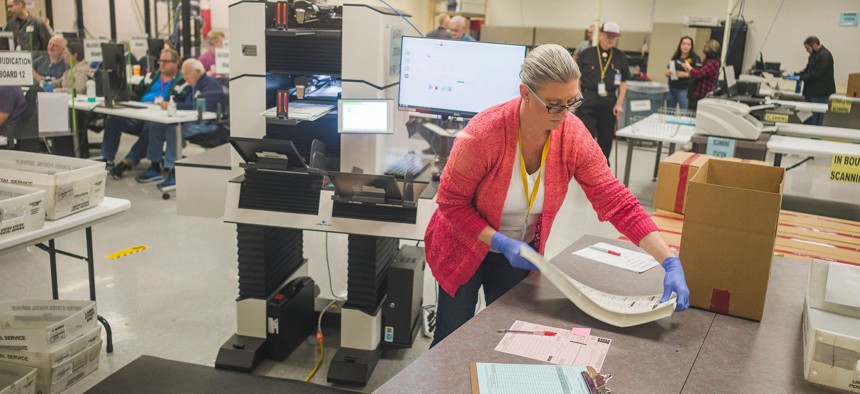 An election worker, watched by observers from both major political parties, handles 2022 midterm ballots in Phoenix, Arizona.