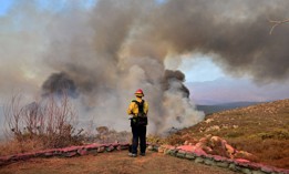 A firefighter working under extreme heat conditions watches as smoke erupts from a hillside fire in Hemet, California in September.
