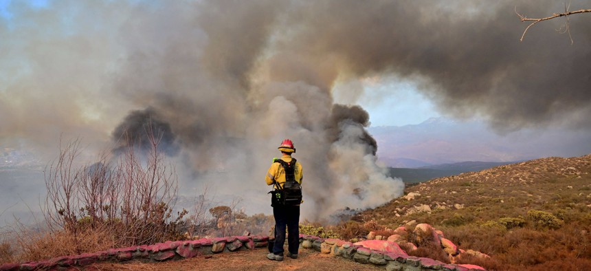 A firefighter working under extreme heat conditions watches as smoke erupts from a hillside fire in Hemet, California in September.