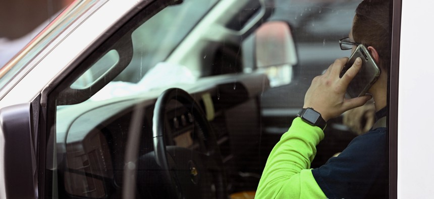 A motorist holds a phone while stopped at a traffic light while driving.