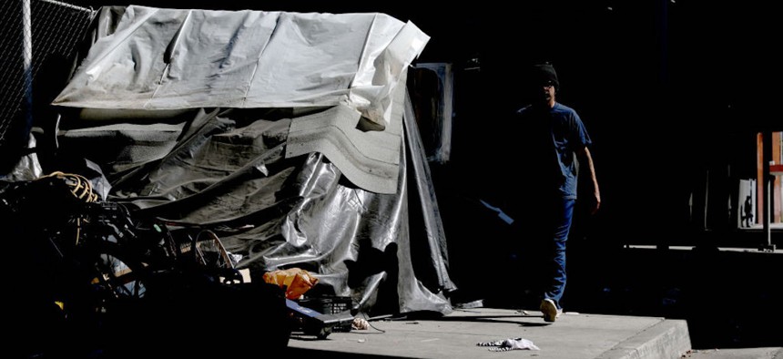 A man walks past a homeless encampment on the sidewalk in Los Angeles, California, on Thursday, July 6, 2023. 
