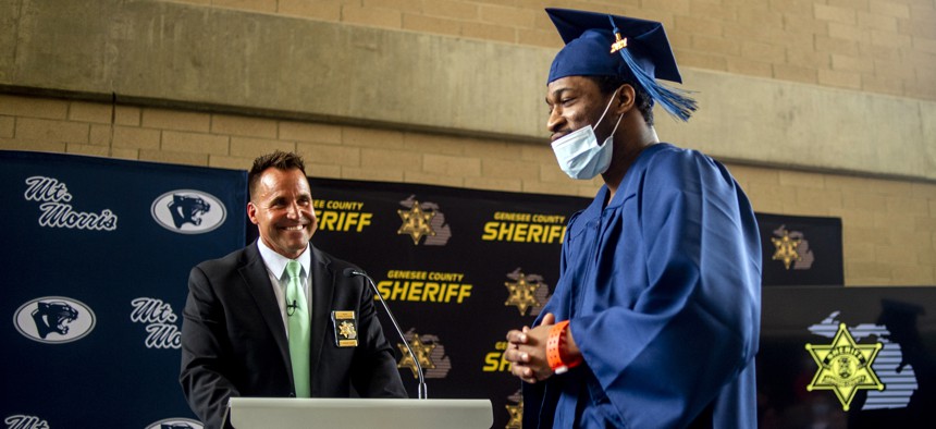 An inmate is presented with his high school diploma by Genesee County Sheriff Christopher R. Swanson during a graduation ceremony attended by the inmate's family.  The diploma was earned under the county's expansive IGNITE education program.