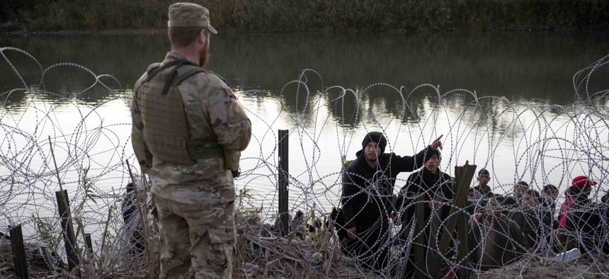  A migrant from Venezuela asks a Texas National guardsman directions to a processing center after crossing from Mexico into the United States in December in Eagle Pass, Texas. A surge of migrants, as many as 12,000 per day, crossing the U.S. southern border has overwhelmed U.S. immigration authorities. 