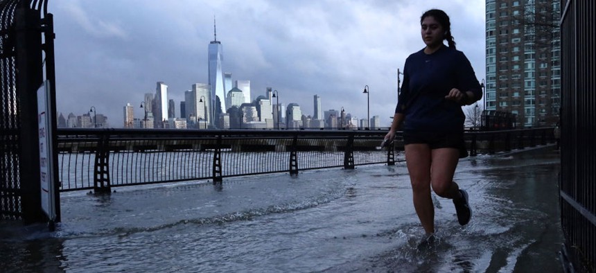Water from the Hudson River overflows a river wall at high tide as a woman jogs in front of the skyline of lower Manhattan in New York City on Jan. 13, 2024, in Jersey City, New Jersey. 