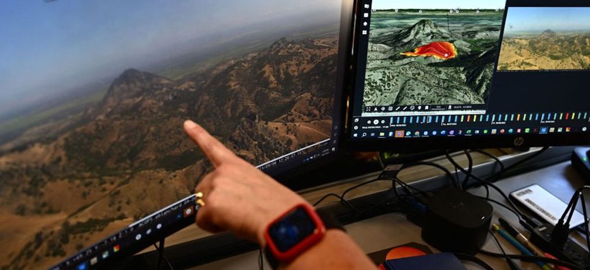 Cal Fire intelligence specialist Suzann Leininger shows fire modeling software viewed alongside a camera feed from the ALERTCalifornia wildfire camera network at Cal Fire's San Diego County headquarters in El Cajon, California, on Sept. 6, 2023. A new monitoring system that uses artificial intelligence to scan for danger helps firefighters quell blazes before they escalate.