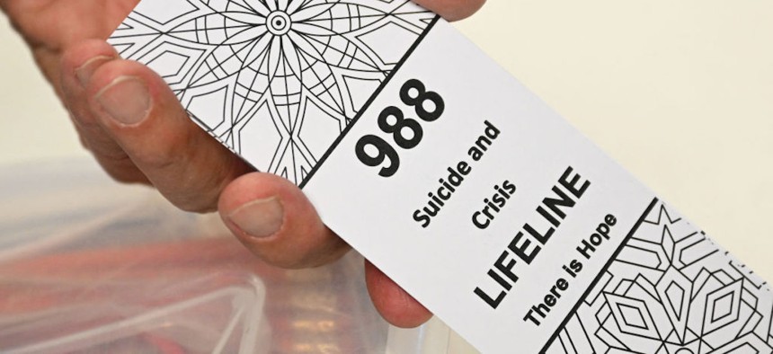 A bookmark for children with the 988 suicide and crisis lifeline emergency telephone number is displayed by Lance Neiberger, a volunteer with the Natrona County Suicide Prevention Task Force, while they speak about mental health and suicide awareness in C
