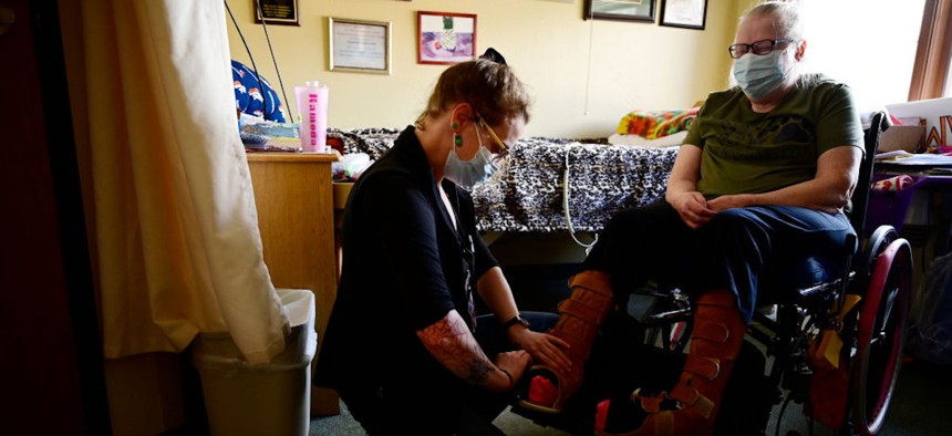  Caregiver Dominique Wansaw helps Ramona Uppendahl wearing the leather feet covers at Good Samaritan Society nursing home in Loveland, Colorado, on Friday, March 4, 2022.