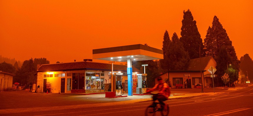 A man rides his bike passed a gas station as smoke fills the sky during the Dixie fire in Greenville, California on July 23, 2021. 