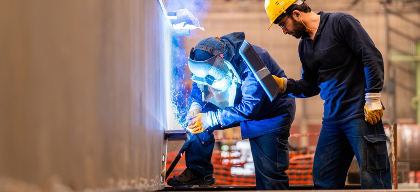 Engineer teaching apprentice to use welding machine