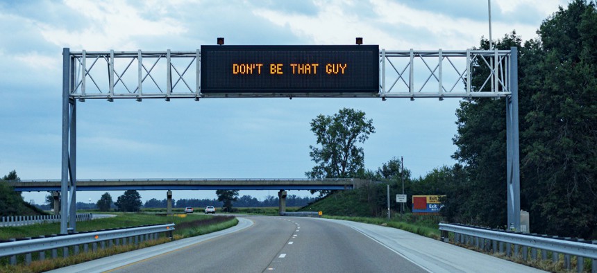 Humorous overhead expressway information road sign - "DON'T BE THAT GUY". This phrase toggles back and forth every few seconds on this digital highway display sign with another message: "NO CAMPING IN THE LEFT LANE" to make a humorous overall message asking slower drivers and motorists to move over into the right lane to allow faster traffic use of the leftmost passing lane.
