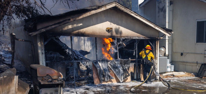 A Riverside City firefighter tries to keep a garage blaze from jumping to the nearby house while battling the Serrano fire on June 24, 2024, in Corona, California.