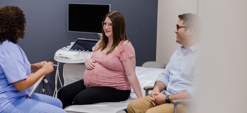 A pregnant patient and their male partner talk to a medical professional in an exam room.