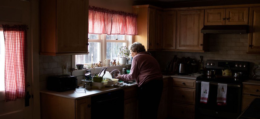 An older individual stands in their kitchen in Chatham, New Hampshire, on March 28, 2022. 