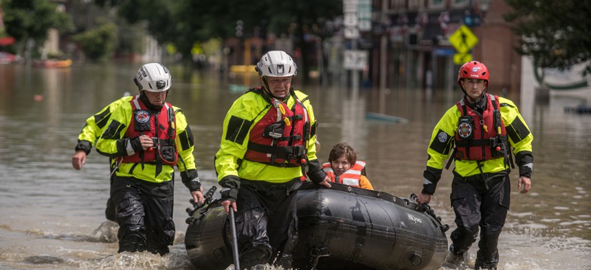 Members of a rescue team evacuate people in downtown Montpelier, Vt., in July 2023 after severe flooding. Vermont enacted a law this year that seeks to charge fossil fuel companies for the damages caused by climate change.