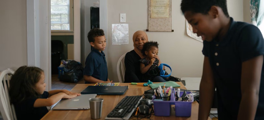 Sameerah Abdullah holds her daughter Maimoonah Abdul Hakeem, 3, while her children Asiyah Jones (left), 6, Dawud Jones, 7, and Musa Moore, 9, do schoolwork in their home in Philadelphia. They are some of the nearly 15,000 Philly students enrolled in cyber charter schools.