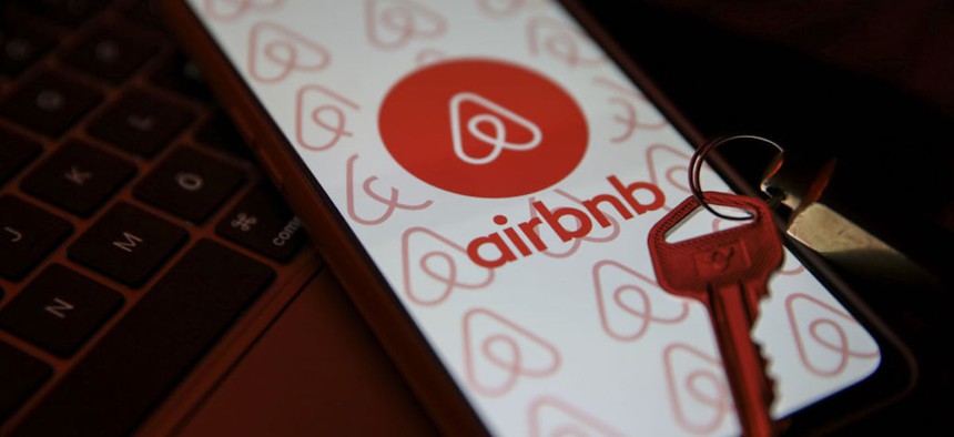 In this photo illustration, a key is seen in front of a mobile phone screen displaying the Airbnb logo.