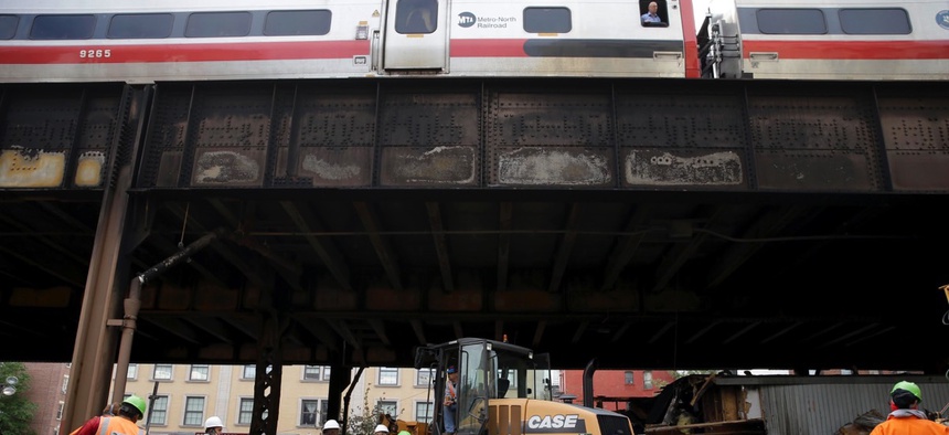 While a Metro-North train passes above, work continues underneath the tracks at the site of a fire in New York on Wednesday.