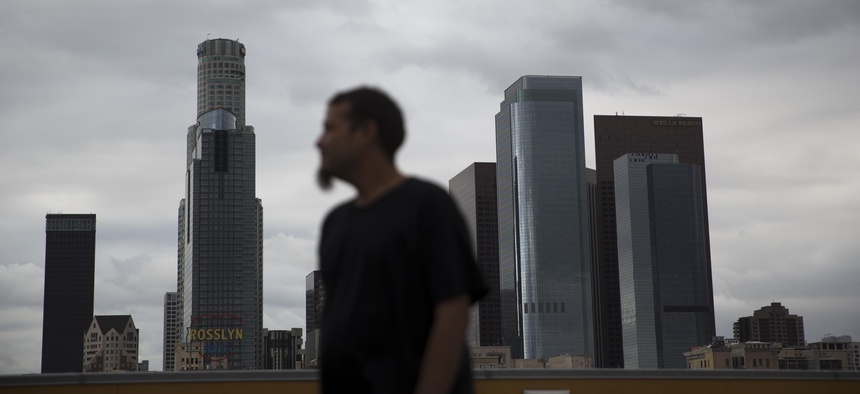 Homeless James Hernandez, a 27-year-old Houston, Texas native, looks away while watching his two daughters play on the rooftop of the Union Rescue Mission as the skyline of downtown Los Angeles is visible in the background, in May 2016.