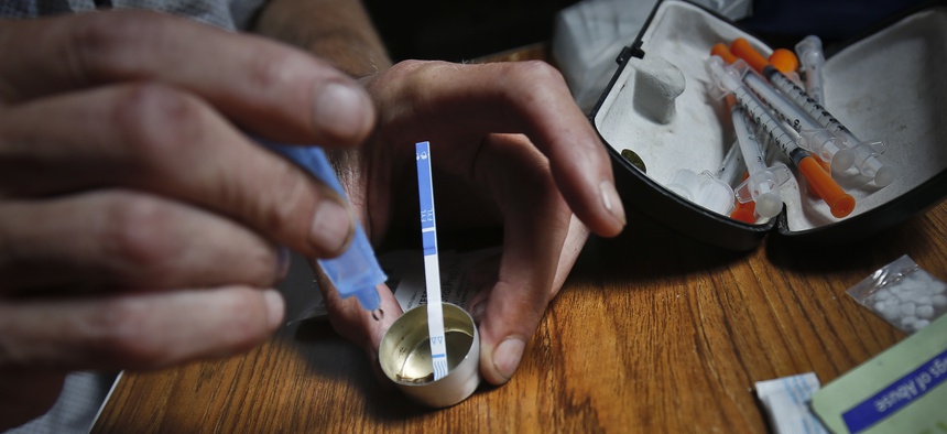 An addict prepares heroin, placing a fentanyl test strip into the mixing container to check for contamination, Wednesday Aug. 22, 2018, in New York. If the strip registers a "pinkish" to red marker then the heroin is positive for contaminants.