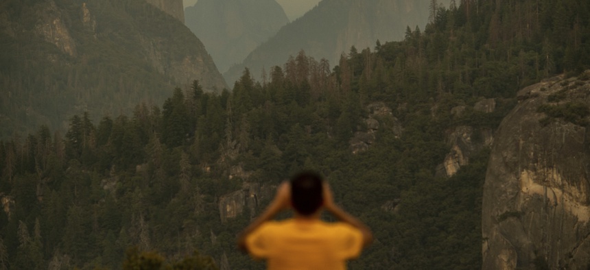In this July 24, 2018, file photo, Francisco Avendano, visiting from Madrid, Spain, photographs Half Dome as smoke from the Ferguson Fire hangs over Yosemite National Park, Calif.