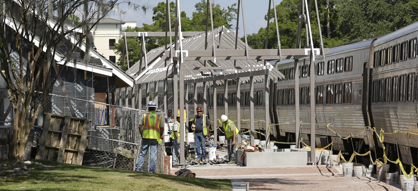 In this Monday, Oct. 28, 2013 photo, construction workers make progress on the SunRail station as an Amtrak train stops at the next door Amtrak station to pick up passengers in Winter Park, Fla.