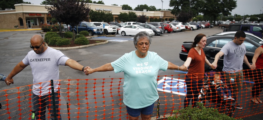In this Saturday, June 1, 2019 file photo, Lisa Dunaway, center, of Virginia Beach, Va., holds hands with other mourners during a vigil in response to a fatal shooting at a municipal building in Virginia Beach, Va.