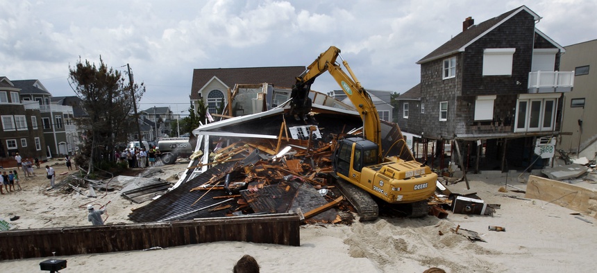 People watch from the beach Wednesday, July 10, 2013, as a home severely damaged by Superstorm Sandy is demolished in the Normandy Beach section of Toms River, N.J.