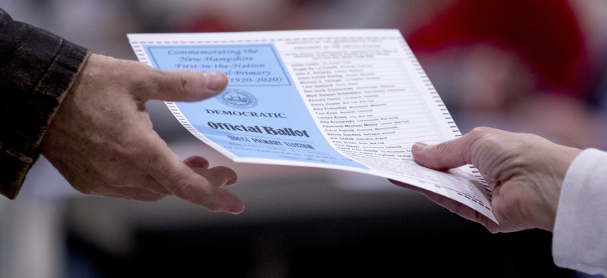A man takes a Democratic ballot to vote in the New Hampshire Primary at Parker-Varney Elementary School, Tuesday, Feb. 11, 2020, in Manchester, N.H.
