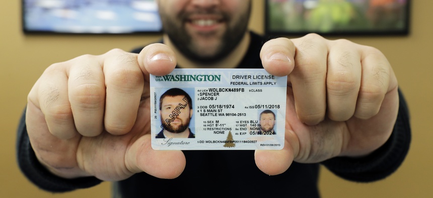Ryan Norris, a license service representative at the Washington state Dept. of Licensing office in Lacey, Wash., poses for a photo Friday, June 22, 2018 while holding a sample copy of a Washington drivers license.