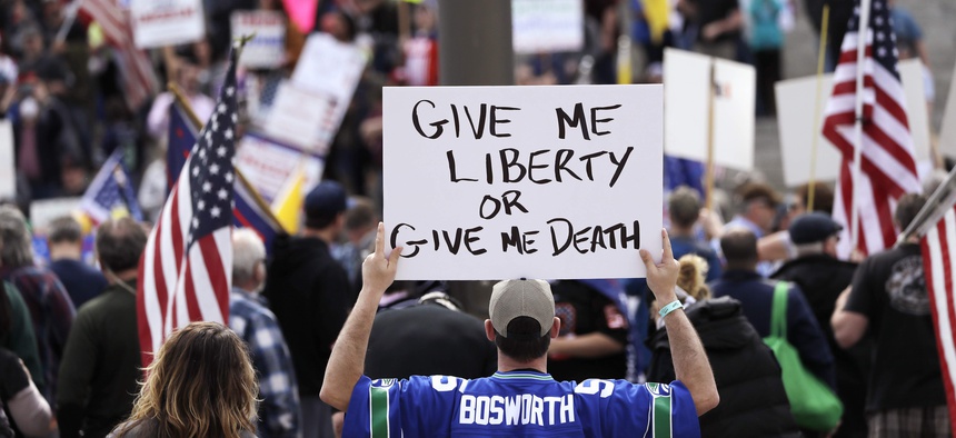 In this April 19, 2020, photo, a man holds a sign in view of the Capitol building at a protest opposing Washington state's stay-home order to slow the coronavirus outbreak in Olympia, Wash.