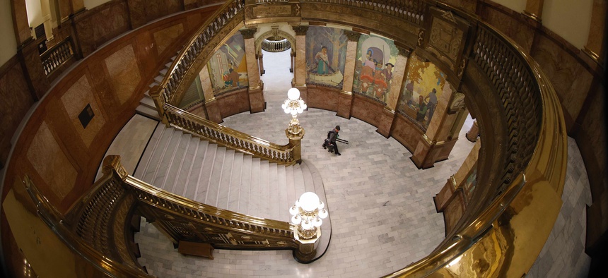 A lone television photographer passes through the rotunda of the State Capitol on the way to a news conference by Gov. Jared Polis to update the state's efforts to control the spread of the new coronavirus Friday, May 15, 2020, in Denver.