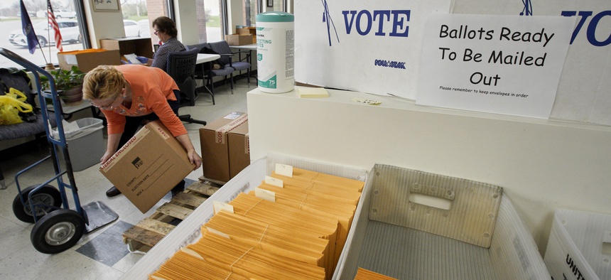 In this April 14, 2020 photo, Nadette Cheney picks up a box of printed ballots as others work on preparing mail-in ballots at the Lancaster County Election Committee offices in Lincoln, Neb.