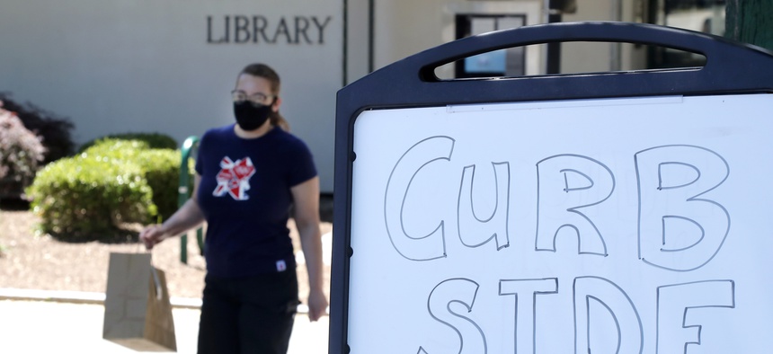Librarian Emily Giguere delivers books to a reader waiting in his car outside the Haverhill Library, Wednesday, June 17, 2020, in Haverhill, Mass. Libraries are closed for interior use due to coronavirus concerns.