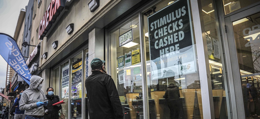In this April 24, 2020, photo, people maintain social distancing and wear face masks due to COVID-19 concerns, while waiting to enter a check cashing service center in the Brooklyn borough of New York.