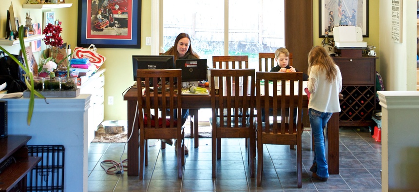 In this Tuesday, March 17, 2020 photo Kim Borton, left, works from home while her children Logan Borton, center, age 6 and Katie Borton, age 7, work on an art project in Beaverton, Ore.