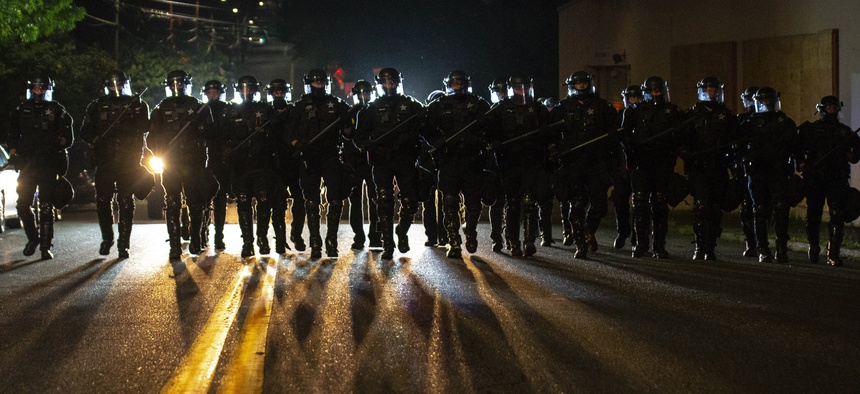 Portland police officers walk through the Laurelhurst neighborhood after dispersing a protest of about 200 people from in front of the Multnomah County Sheriff's Office early in the morning on Saturday, Aug. 8, 2020 in Portland, Ore.