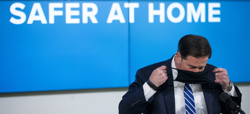 Arizona Gov. Doug Ducey puts on his face mask during a news conference about the coronavirus, Thursday, July 16, 2020, in Phoenix. (Cheryl Evan/The Arizona Republic via AP, Pool)