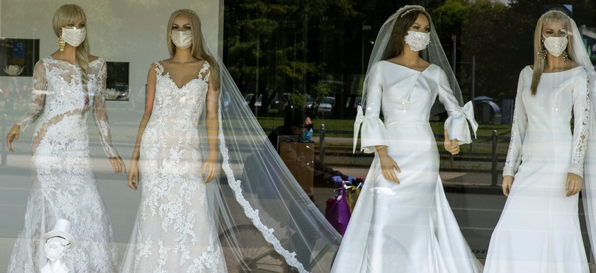 A cyclist wearing a protective mask to protect against coronavirus is reflected in the window of a wedding dress store with mannequins wearing face masks on Thursday, April 23, 2020.