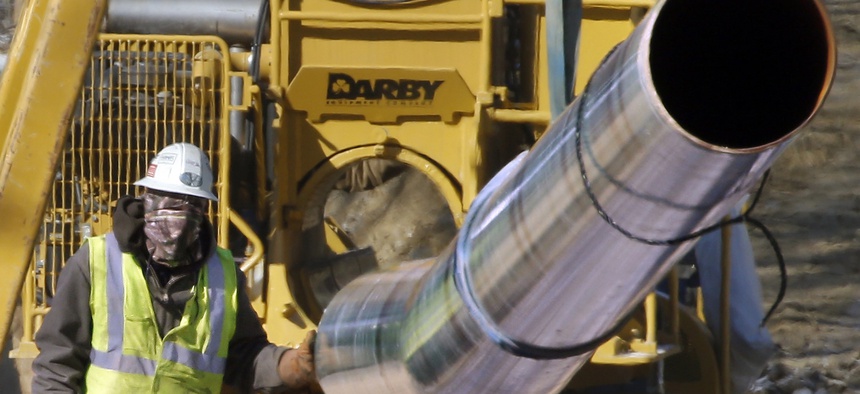 In this Feb. 13, 2015, file photo, a worker shields his face against temperatures in the teens as he guides a section of pipe while working on a shale gas pipe line in Zelienople, Pa.