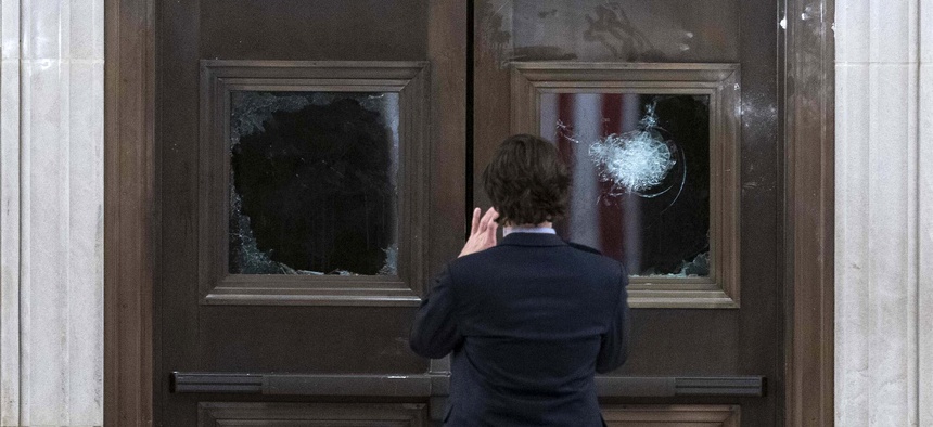 In this Jan. 7, 2021, file photo a man takes a photo of broken windows near the Rotunda in the early morning hours after insurrectionist loyal to President Donald Trump stormed the Capitol in Washington.